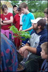 Matthew Logan shows young students how to properly plant a tree